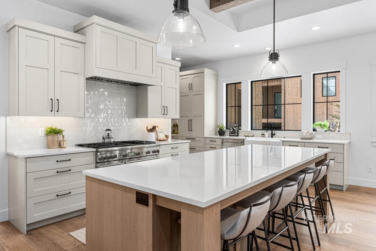 Two tone kitchen with light wood-type flooring, two tone cabinets, a large island, light stone countertops, and a breakfast bar area