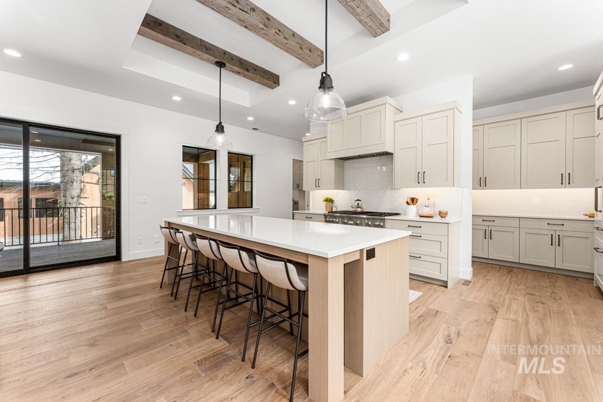 Kitchen featuring beamed ceiling, decorative backsplash, a large island, hanging light fixtures, and a kitchen breakfast bar