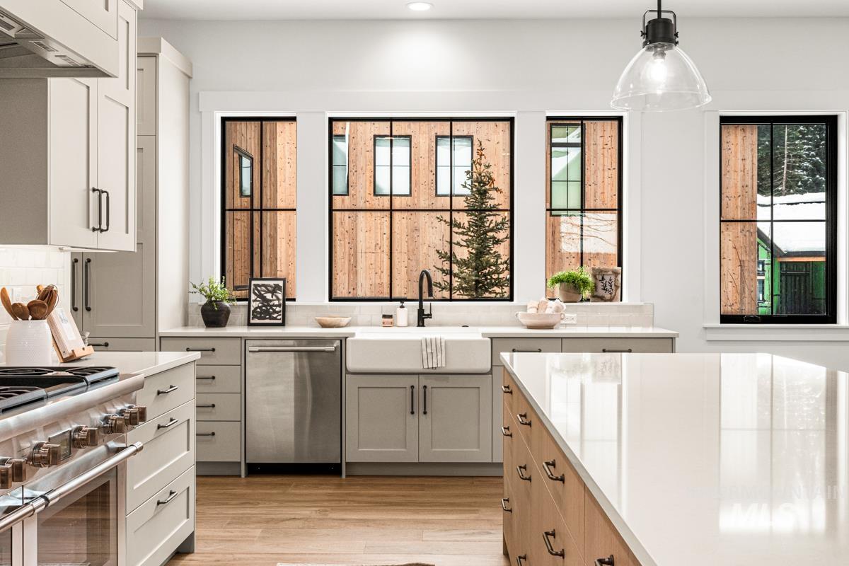 Two tone kitchen with stainless steel appliances, dual tone cabinets, pendant lighting, light wood-type flooring, and light stone counters