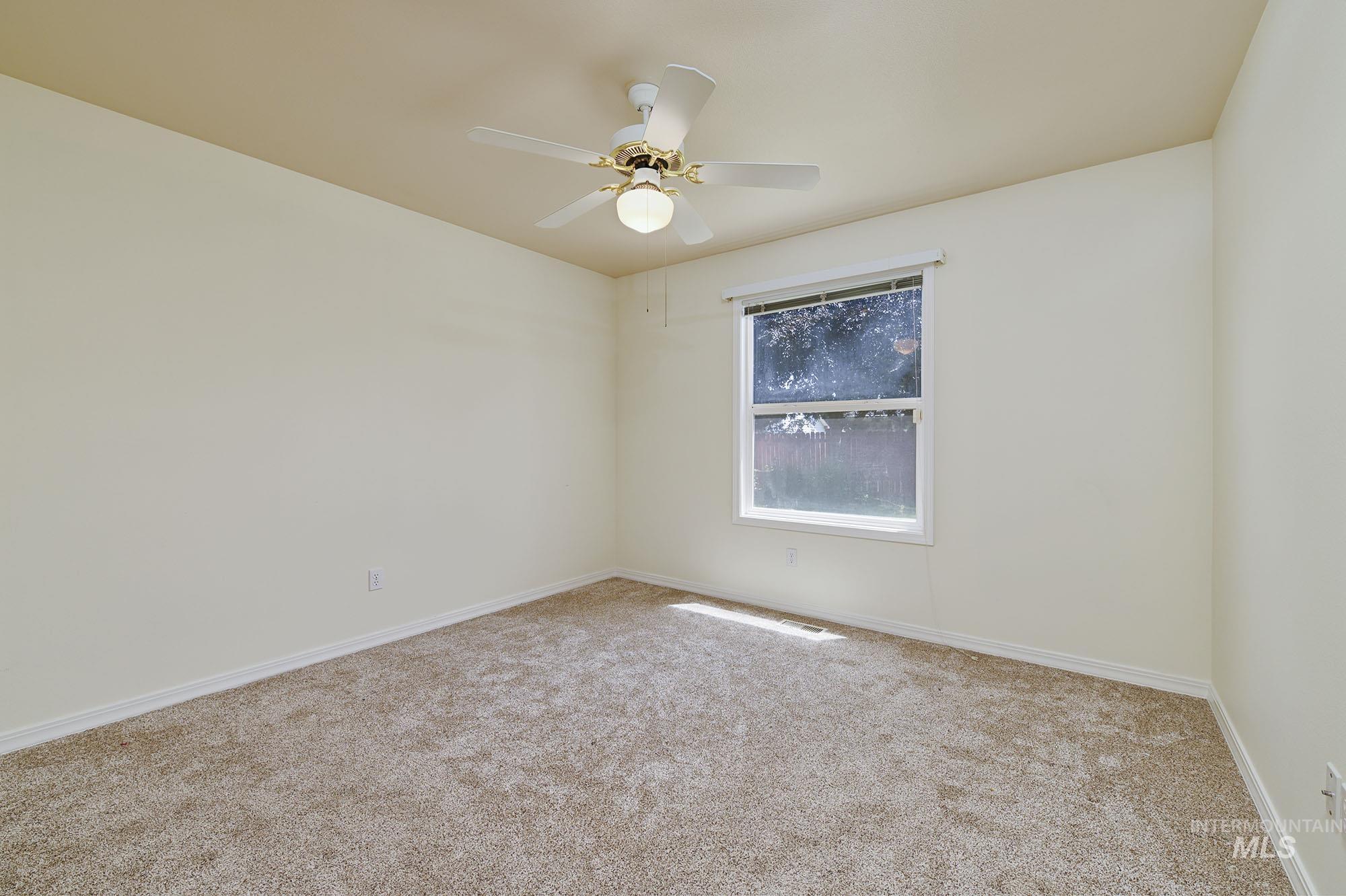 Carpeted room featuring a single window, white trim, and a ceiling fan with integrated lighting