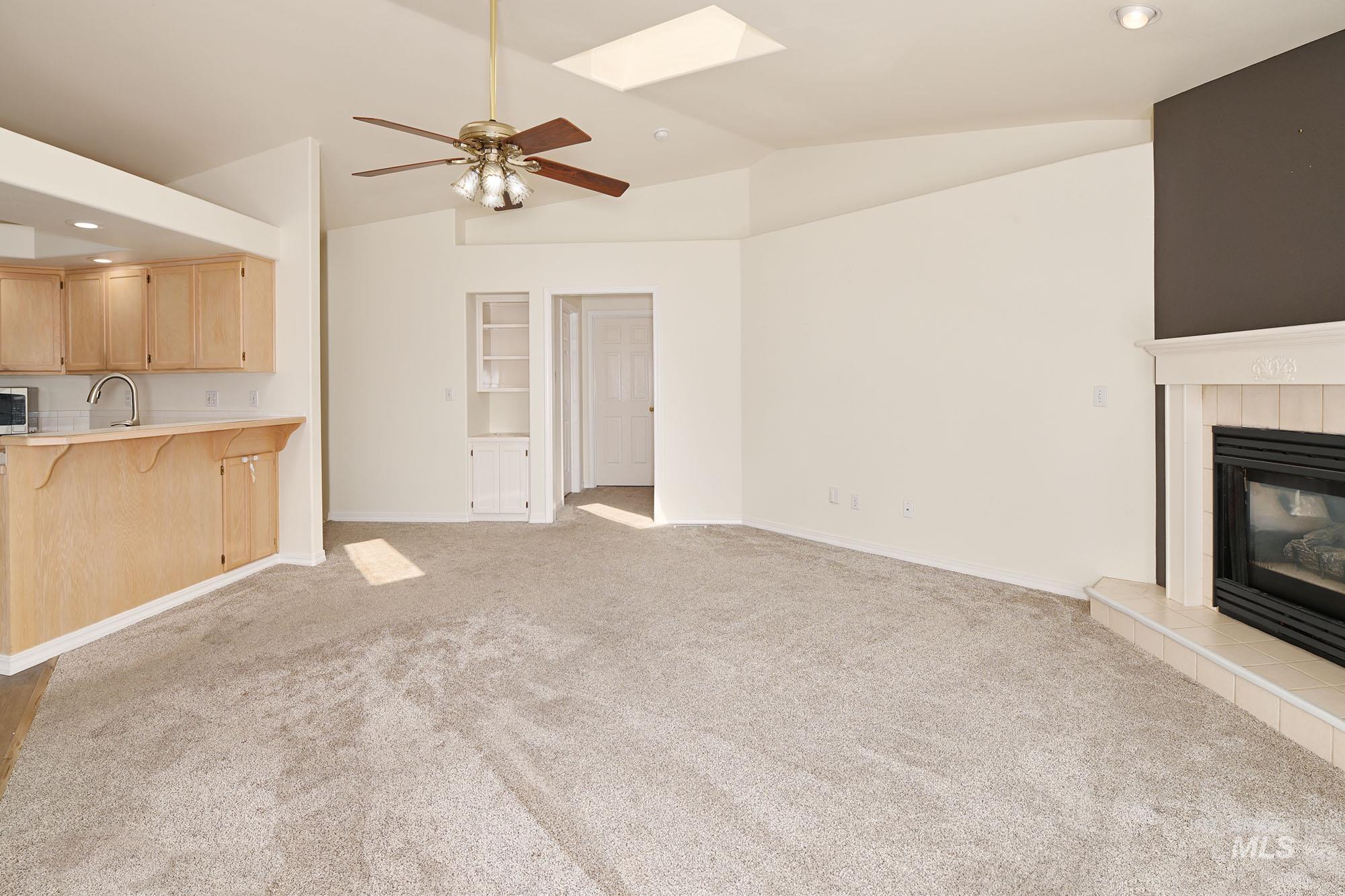 Vaulted ceiling living area featuring a ceiling fan, central fireplace with tile surround, skylight, and built-in shelving