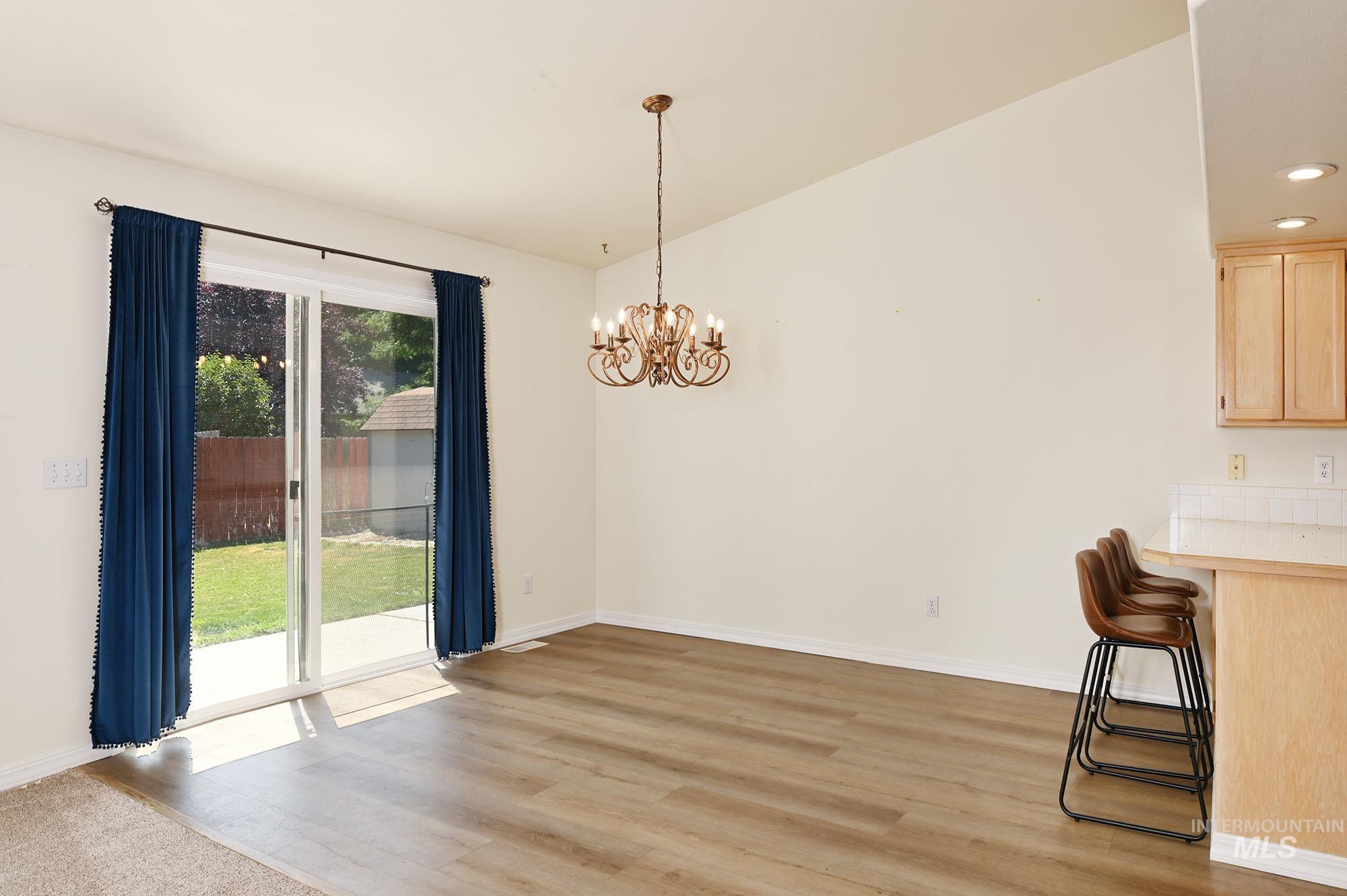 Spacious room featuring wood-finish flooring, a vaulted ceiling, and an ornate chandelier
