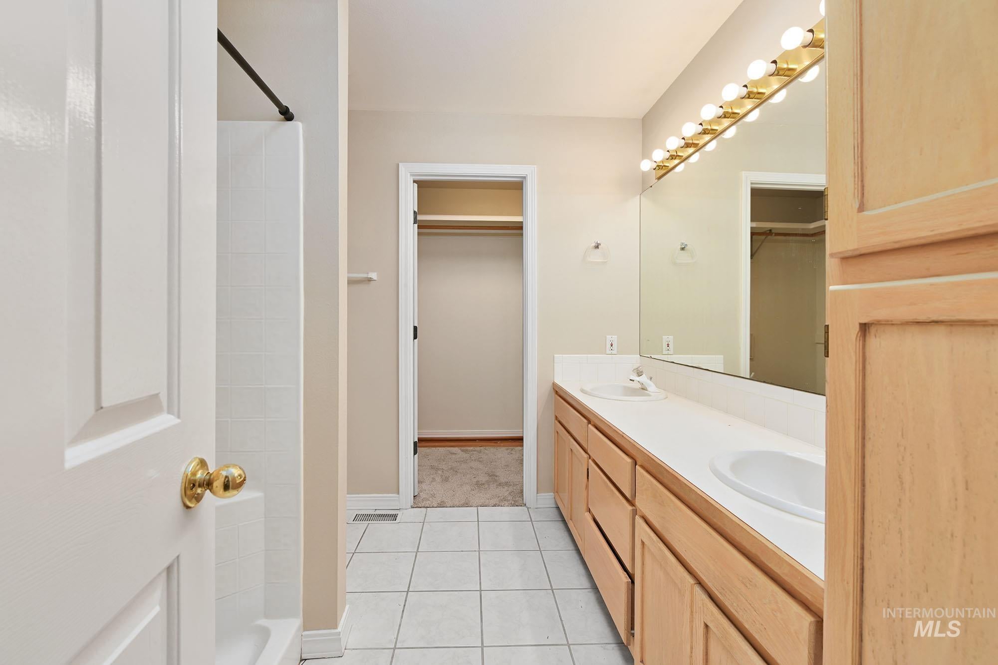 Bathroom featuring a double vanity with light wood cabinetry, dual integrated sinks, and a full-width mirror with overhead bar lighting