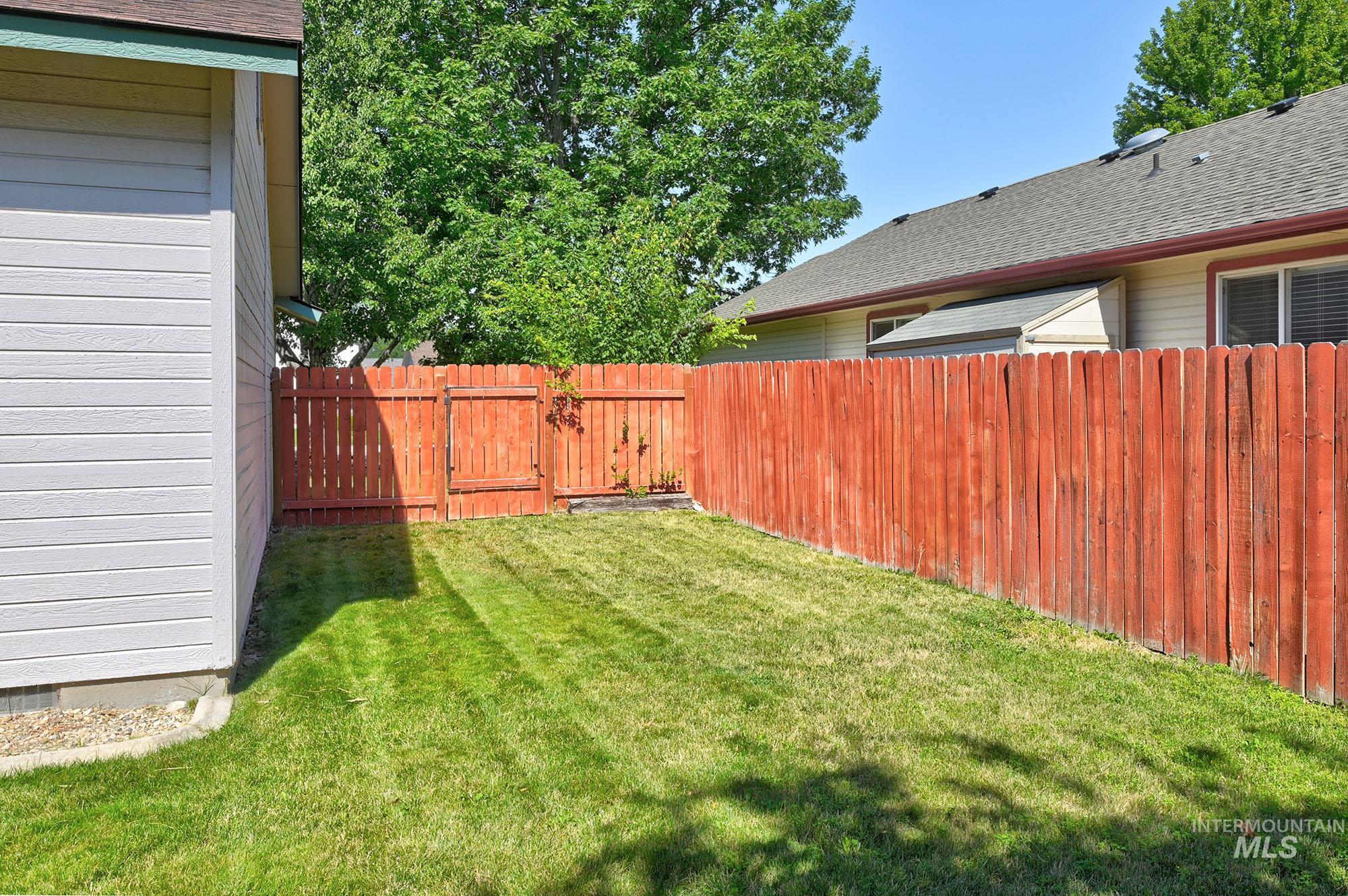 Grassed yard area featuring a red-stained wood privacy fence with gate access