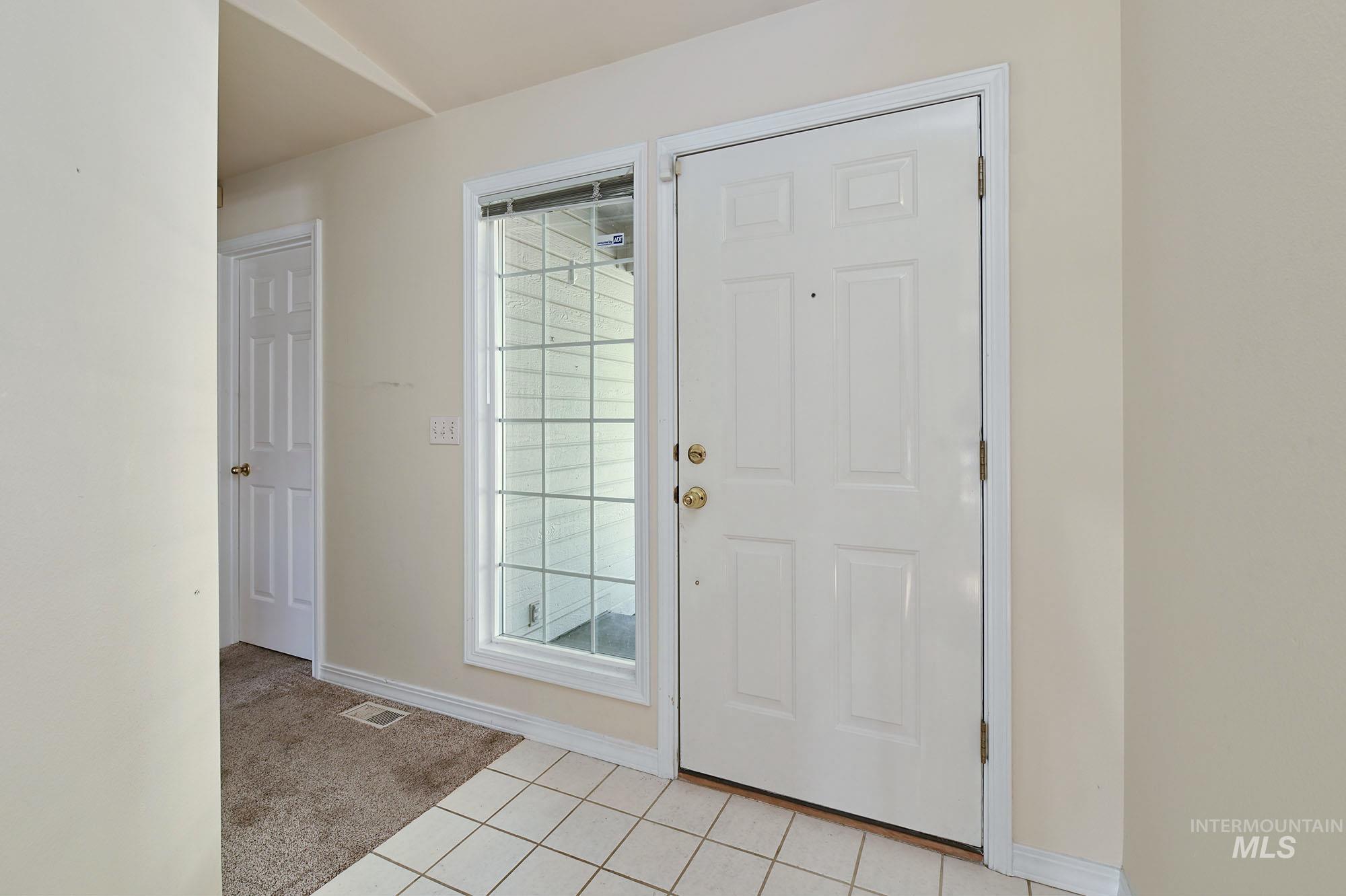 Entryway featuring a white paneled door, a sidelight window with grid details, and tile flooring