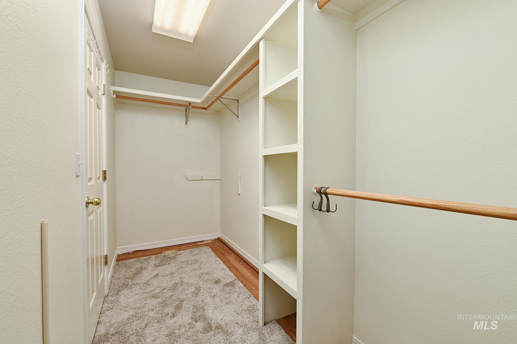 Spacious walk-in closet featuring built-in shelving, multiple hanging rods, and a door with brass-finish hardware