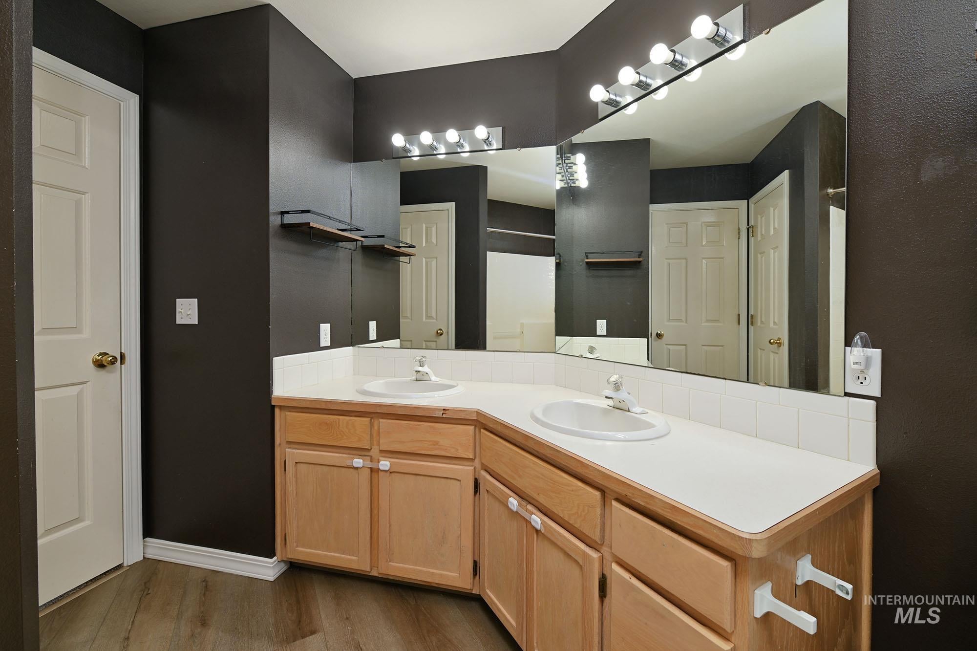 Dual vanity featuring white countertops, light wood-finish cabinetry, and integrated sinks
