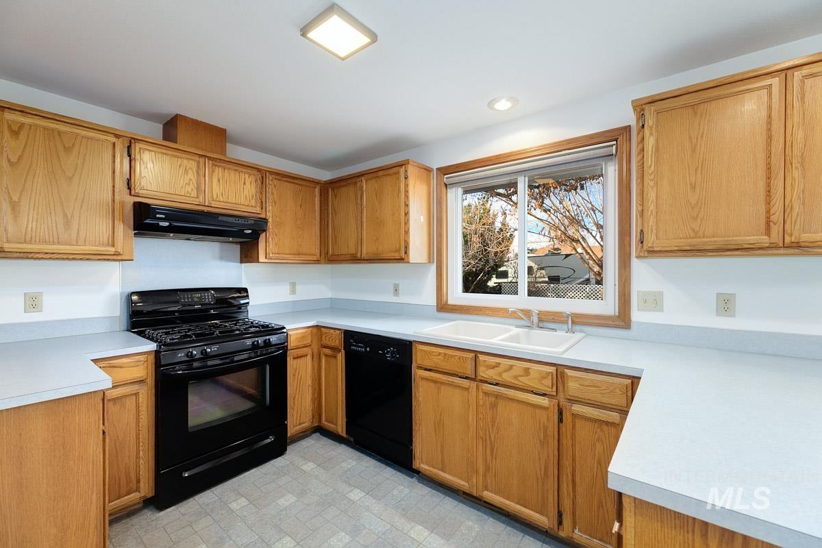 Kitchen with black appliances, light countertops, under cabinet range hood, and brown cabinetry