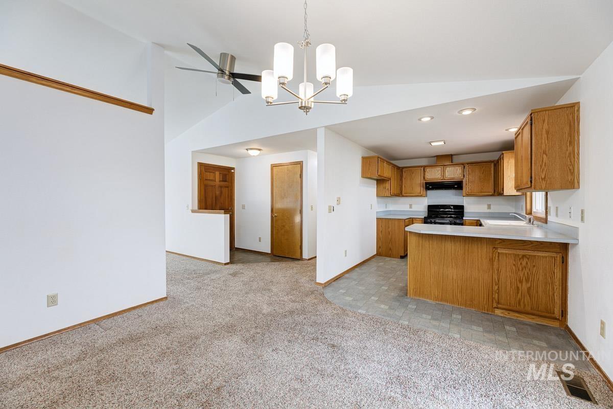 Kitchen with light countertops, a peninsula, a chandelier, brown cabinetry, and decorative light fixtures