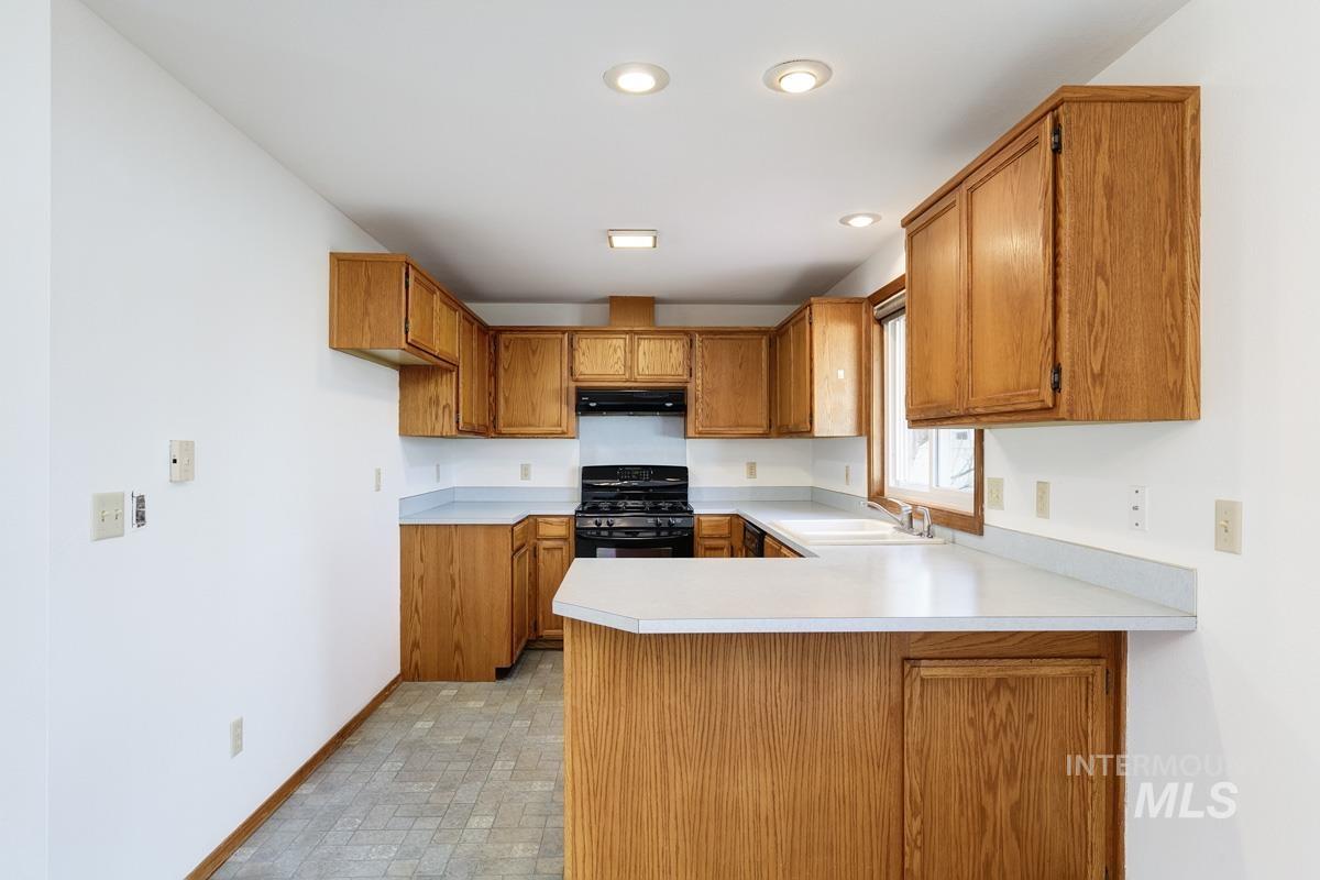 Kitchen featuring brown cabinets, black gas range oven, light countertops, a peninsula, and under cabinet range hood