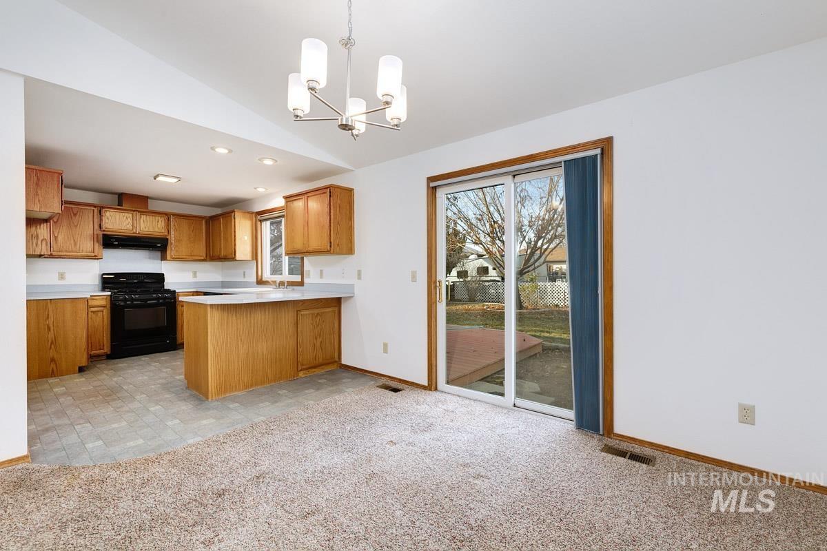 Kitchen with light countertops, black gas range oven, a chandelier, a peninsula, and light carpet