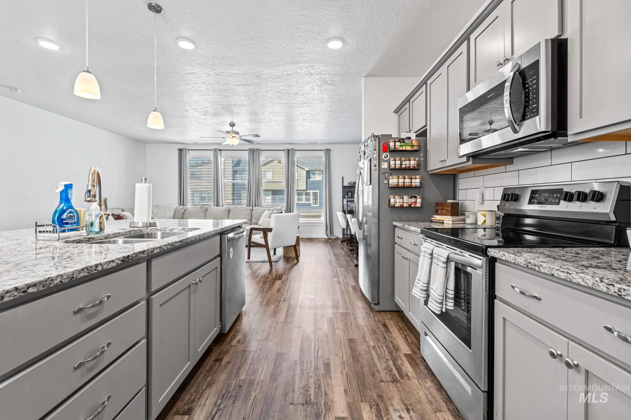Kitchen featuring appliances with stainless steel finishes, gray cabinets, dark wood-style floors, a textured ceiling, and a ceiling fan