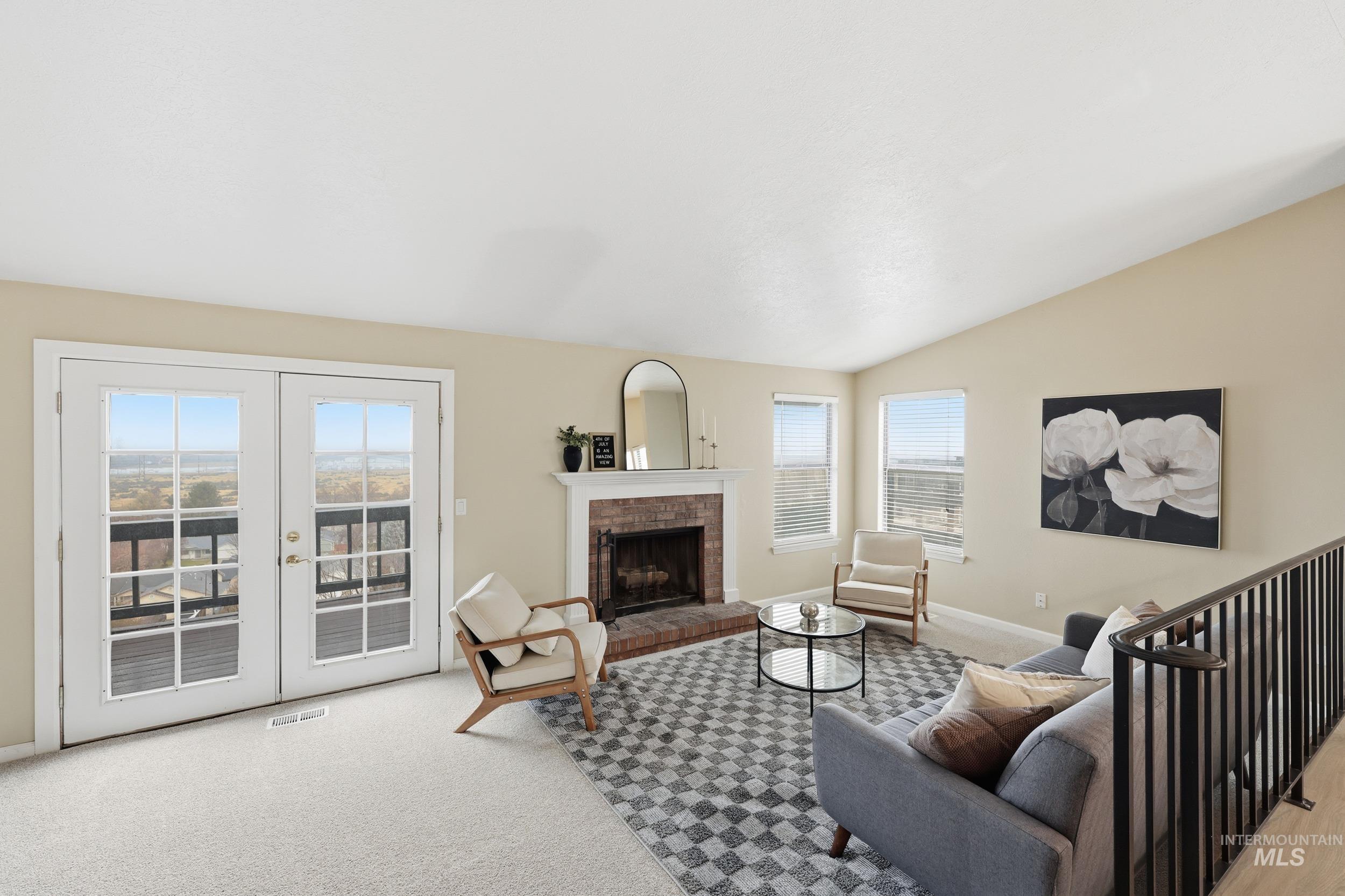 Living room featuring a brick fireplace, lofted ceiling, light colored carpet, and french doors