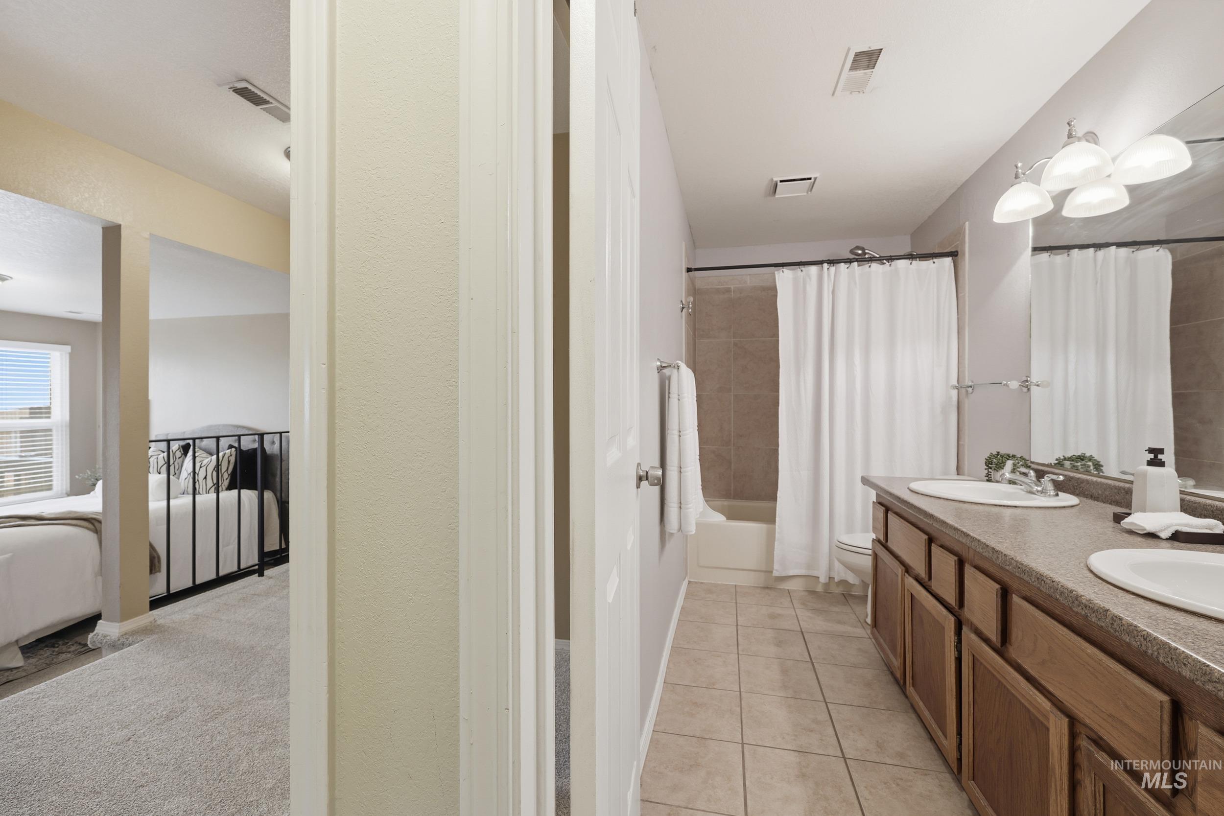 Bathroom featuring double vanity, shower / tub combo, and light tile patterned flooring