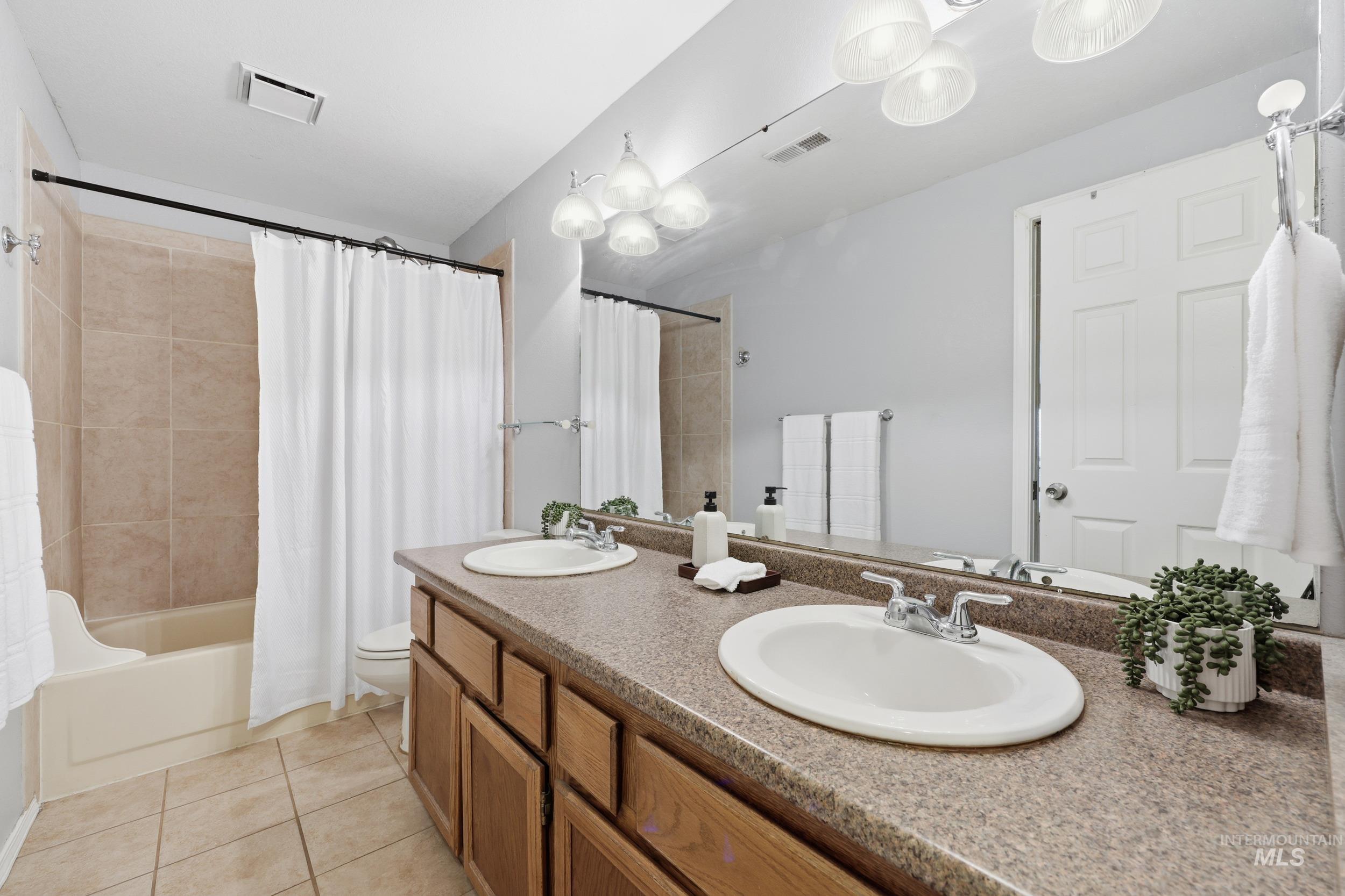 Full bathroom featuring double vanity, shower / tub combo, and light tile patterned floors