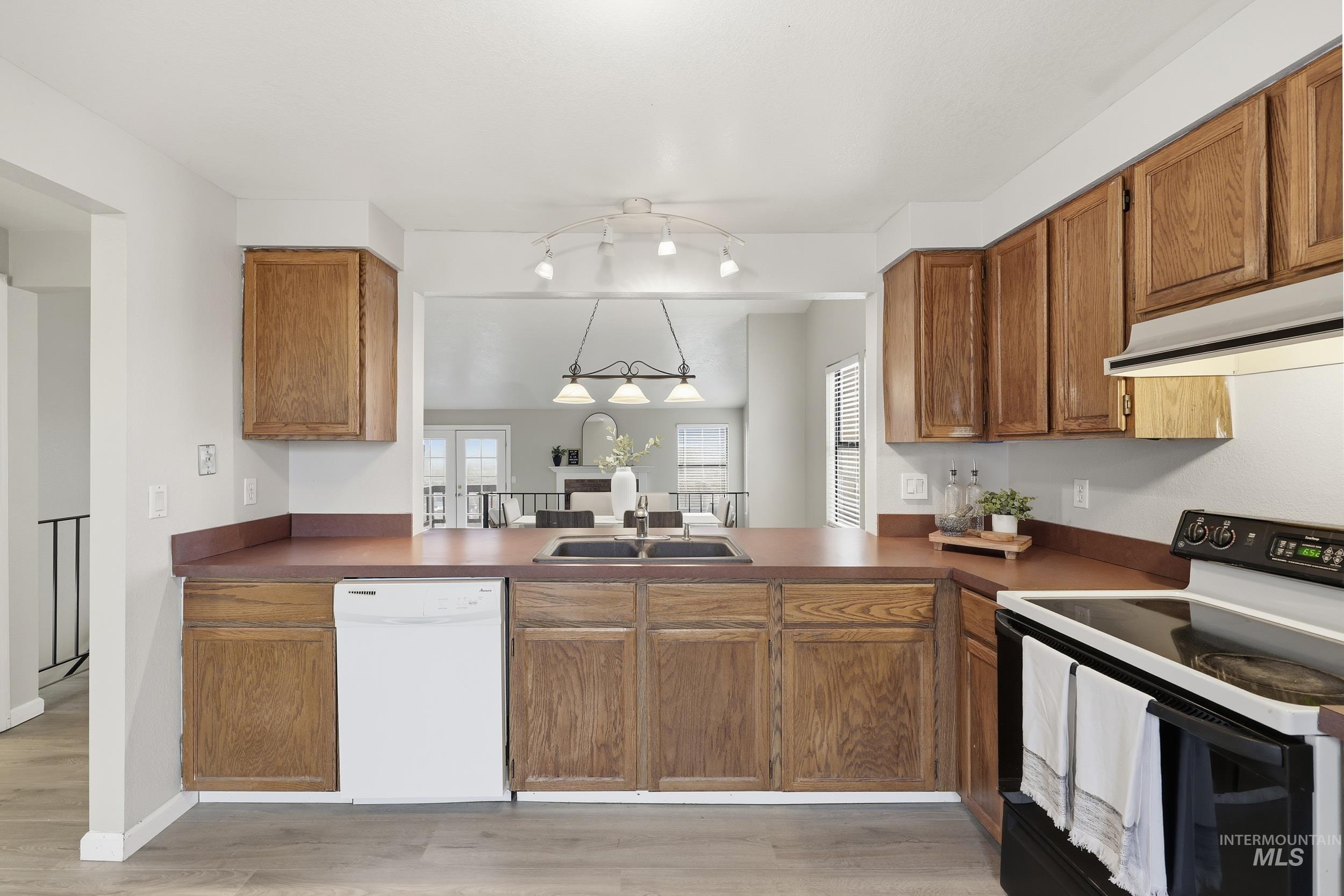 Kitchen featuring electric stove, white dishwasher, range hood, and brown cabinets