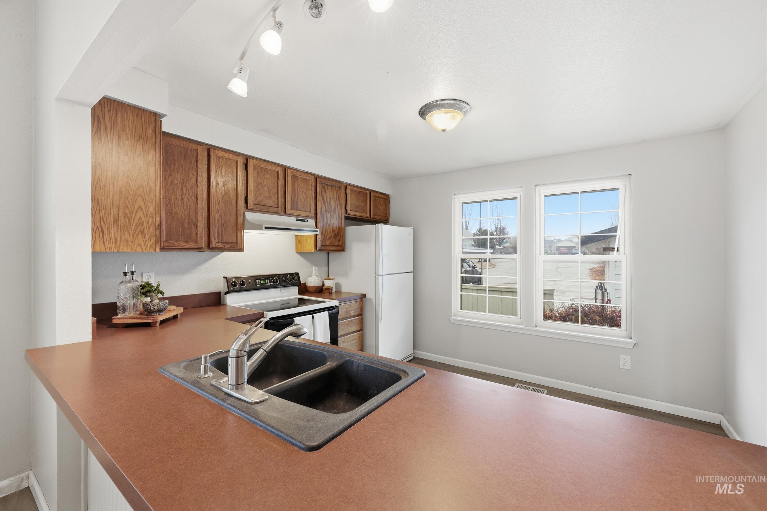 Kitchen featuring white appliances, brown cabinets, under cabinet range hood, and a peninsula
