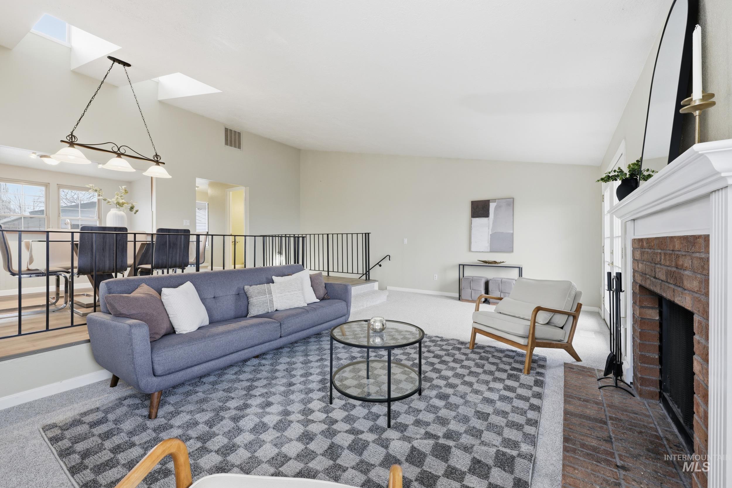 Carpeted living room featuring vaulted ceiling, plenty of natural light, a skylight, and a brick fireplace