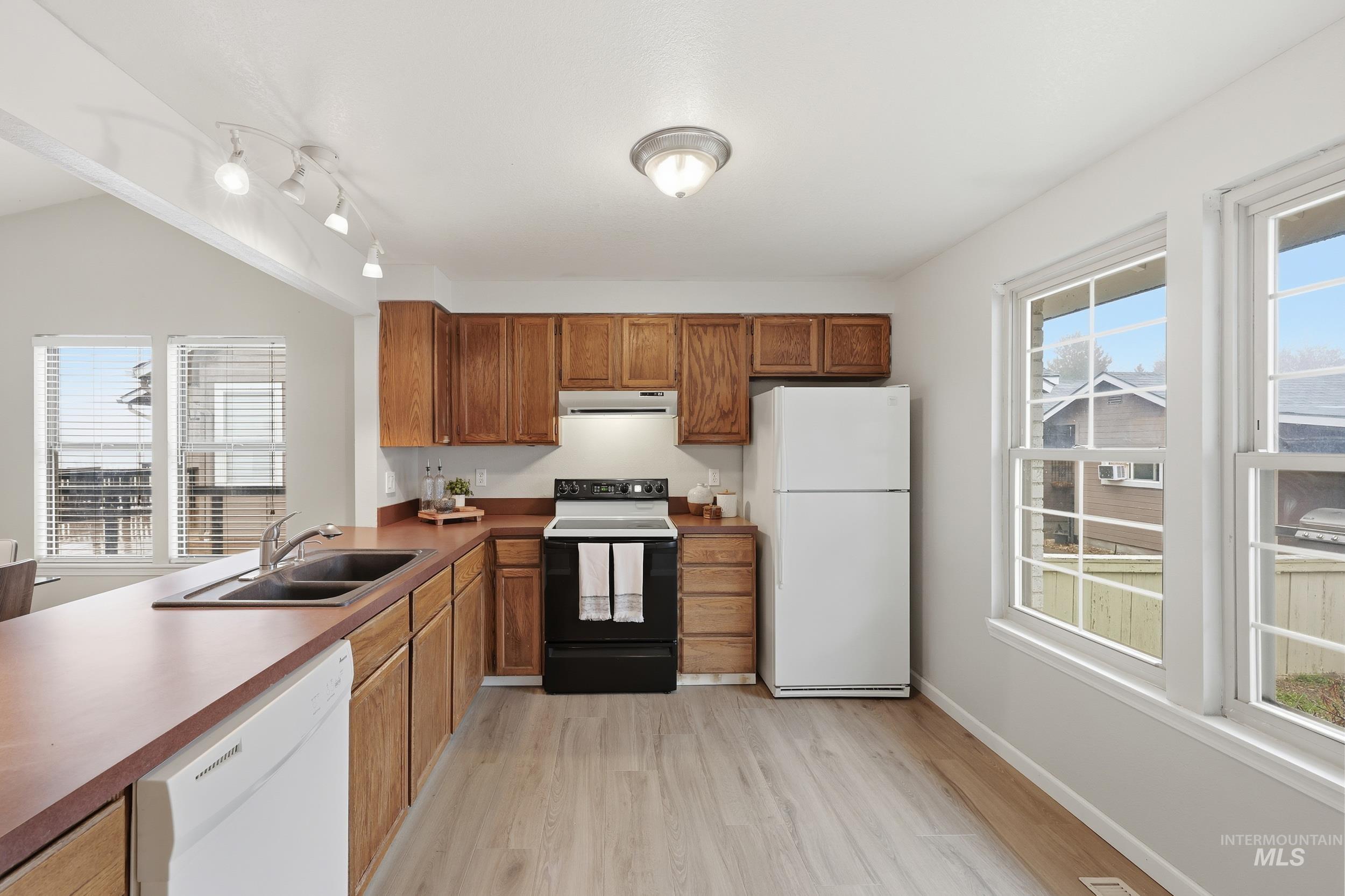 Kitchen featuring white appliances, healthy amount of natural light, light wood-type flooring, and under cabinet range hood
