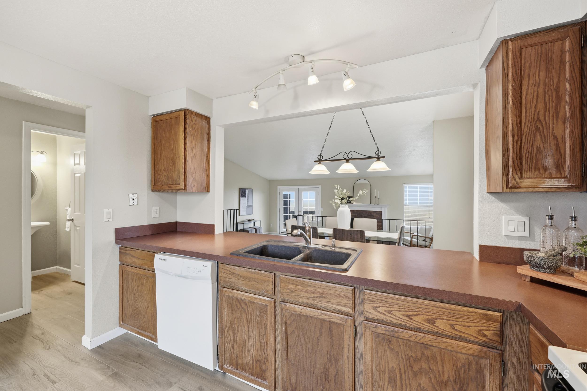 Kitchen with white appliances, lofted ceiling, dark countertops, brown cabinetry, and light wood-type flooring