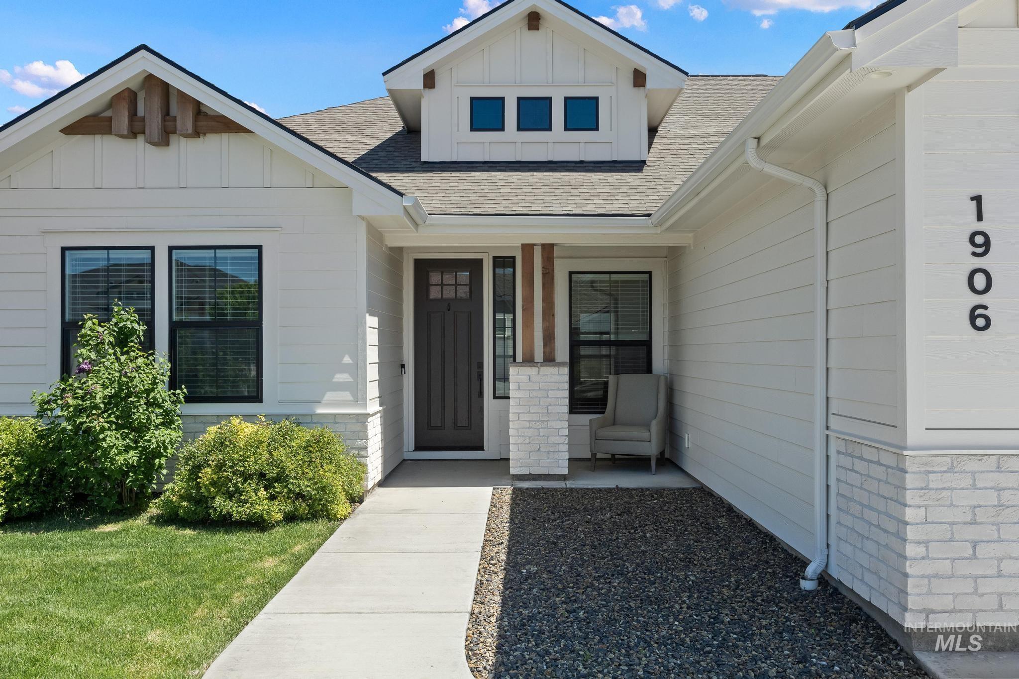 Contemporary white siding exterior featuring a covered entry, dark paneled front door, white brick accents, and a dormer with three windows