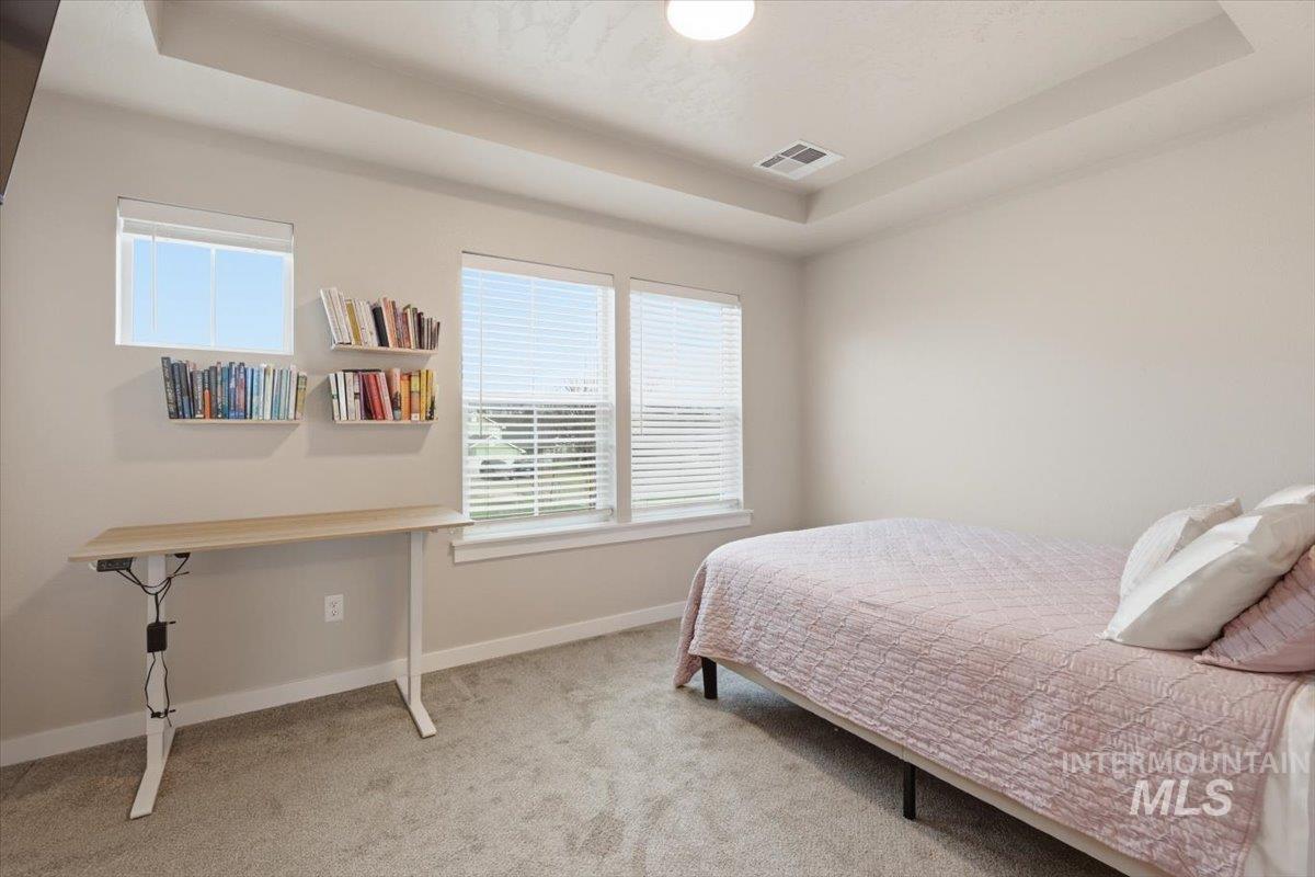 Bedroom with a tray ceiling and light colored carpet