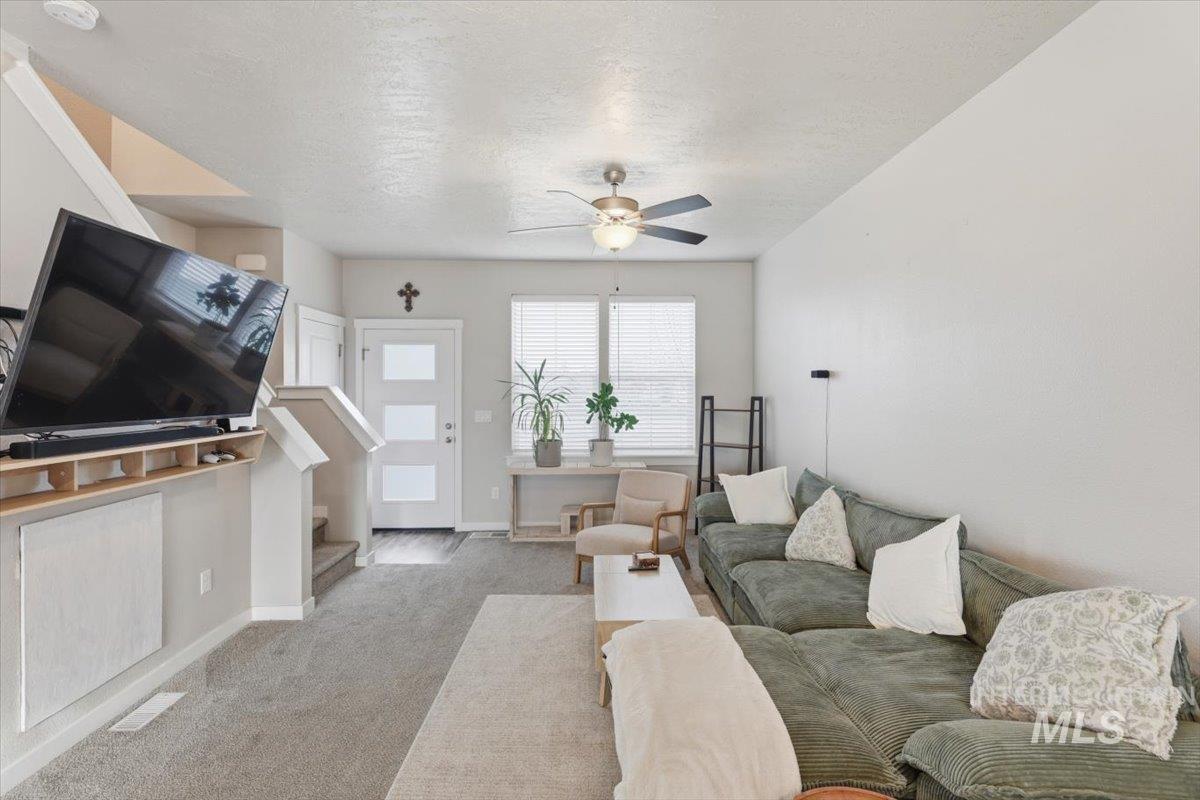 Living area with a ceiling fan, a textured ceiling, and light carpet