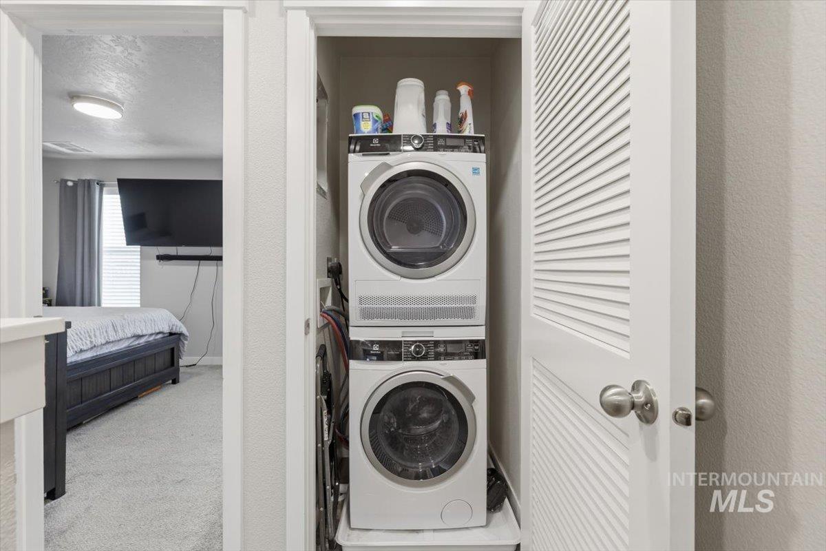 Laundry area featuring light carpet, stacked washer / drying machine, and a textured ceiling