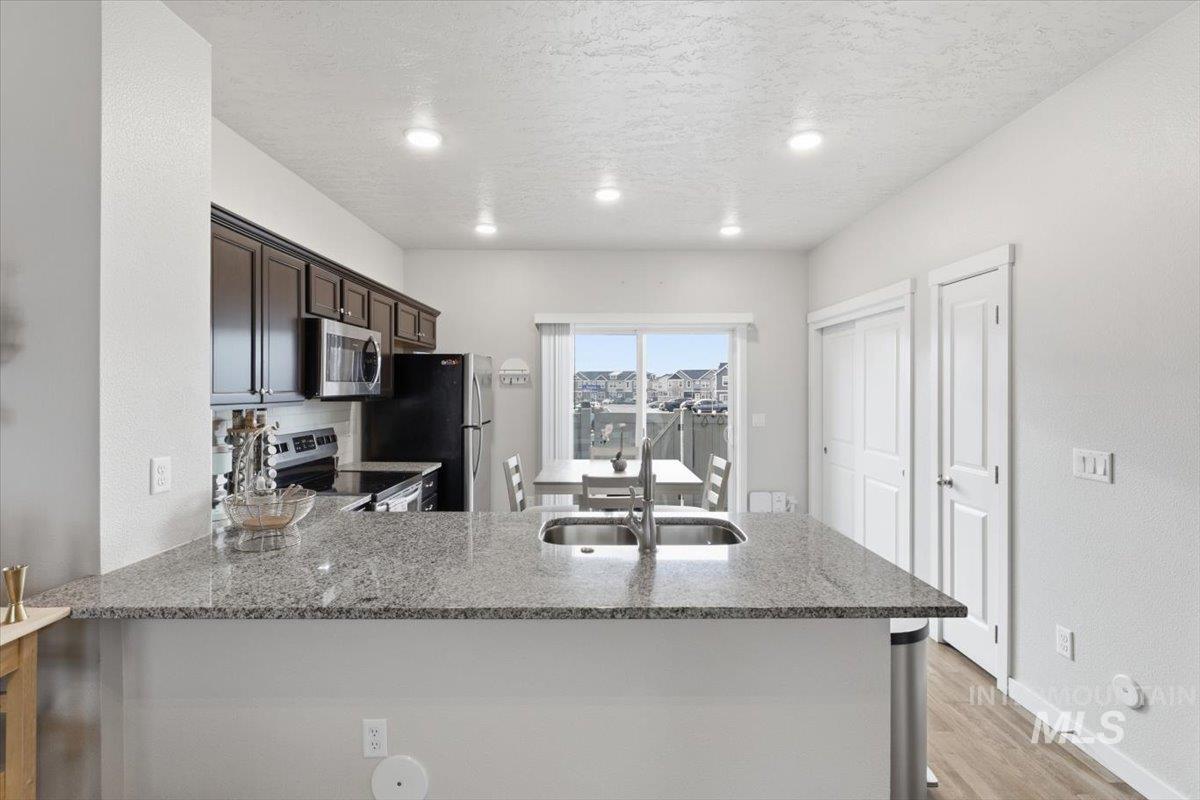 Kitchen with a peninsula, stainless steel appliances, a textured ceiling, light stone countertops, and light wood-style flooring