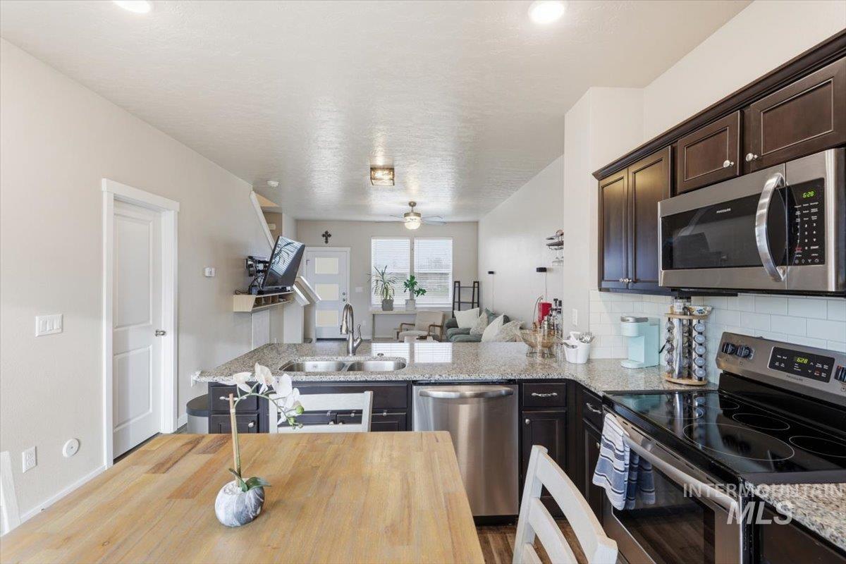 Kitchen with stainless steel appliances, a peninsula, dark wood finish cabinetry, open floor plan, and light stone counters
