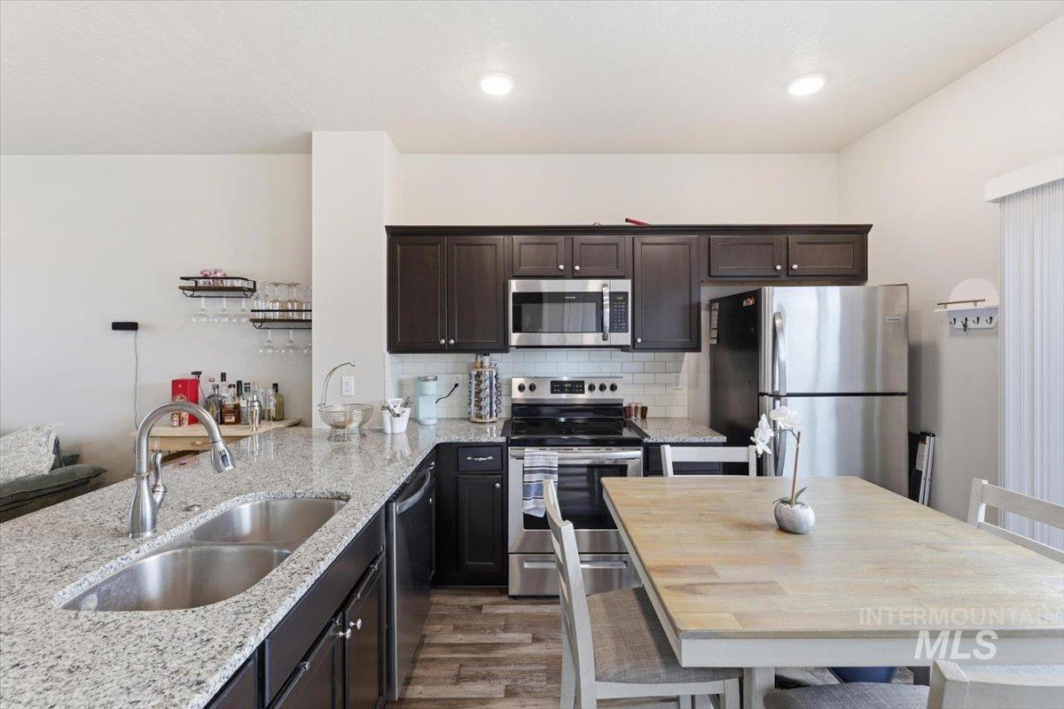 Kitchen featuring stainless steel appliances, dark wood finish cabinetry, light stone counters, and light wood-type flooring