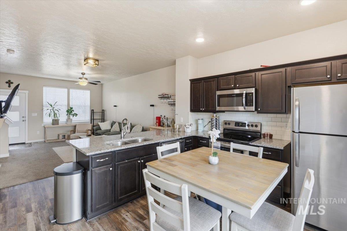 Kitchen featuring stainless steel appliances, dark wood finish cabinets, open floor plan, a peninsula, and light stone counters
