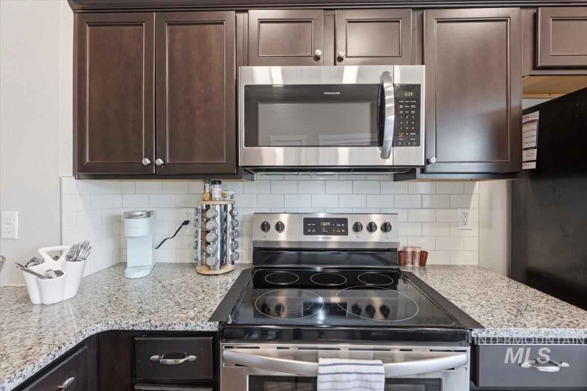 Kitchen with dark wood finish cabinets, stainless steel appliances, light stone countertops, and backsplash