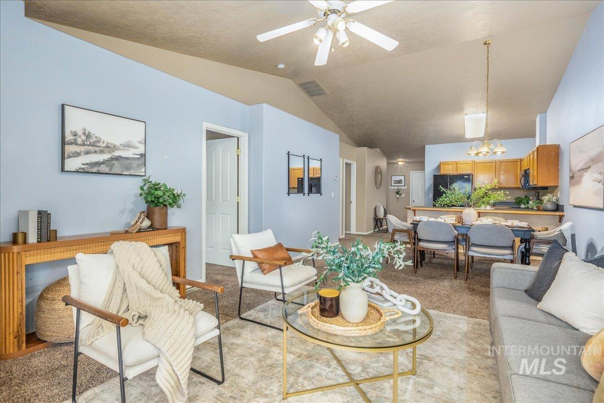 Living room featuring light colored carpet, a ceiling fan, lofted ceiling, a chandelier, and a textured ceiling