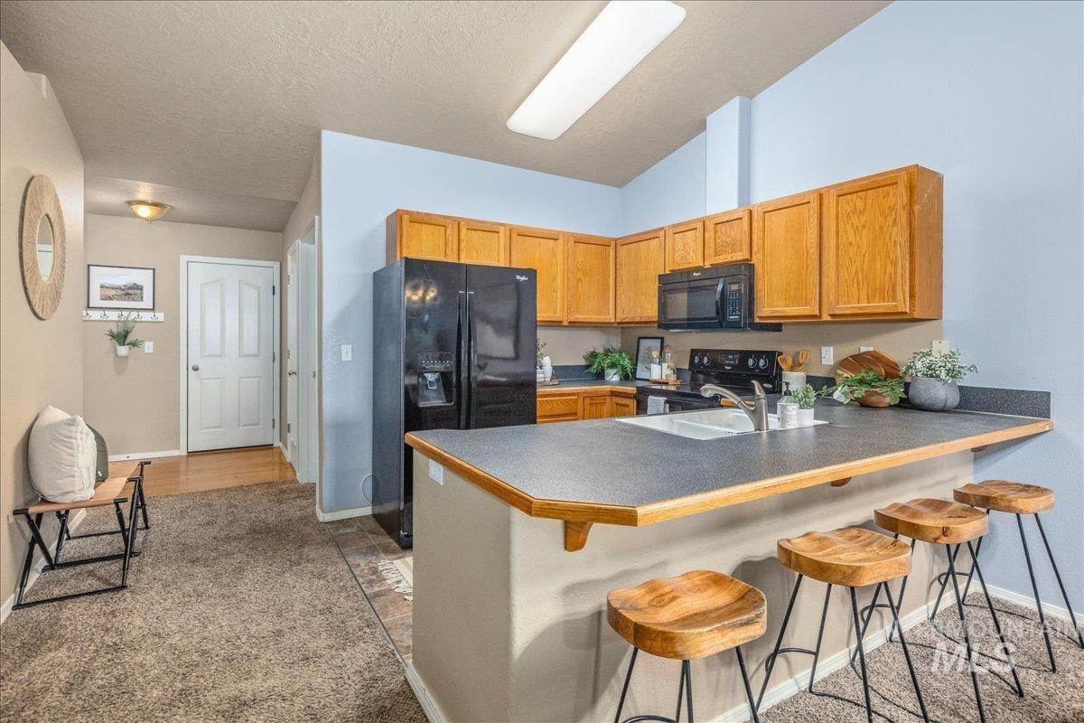 Kitchen with black appliances, a kitchen breakfast bar, dark countertops, light colored carpet, and a textured ceiling