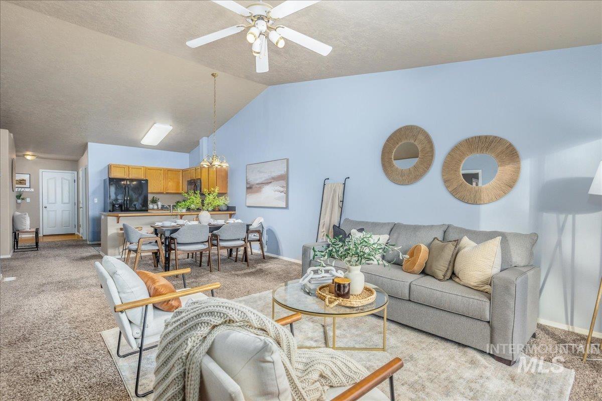 Living area with light carpet, a chandelier, vaulted ceiling, a ceiling fan, and a textured ceiling