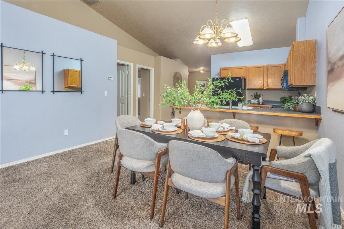 Dining area featuring a chandelier, light colored carpet, and vaulted ceiling