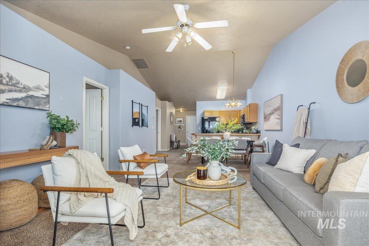 Living room featuring vaulted ceiling, ceiling fan, light carpet, and a chandelier