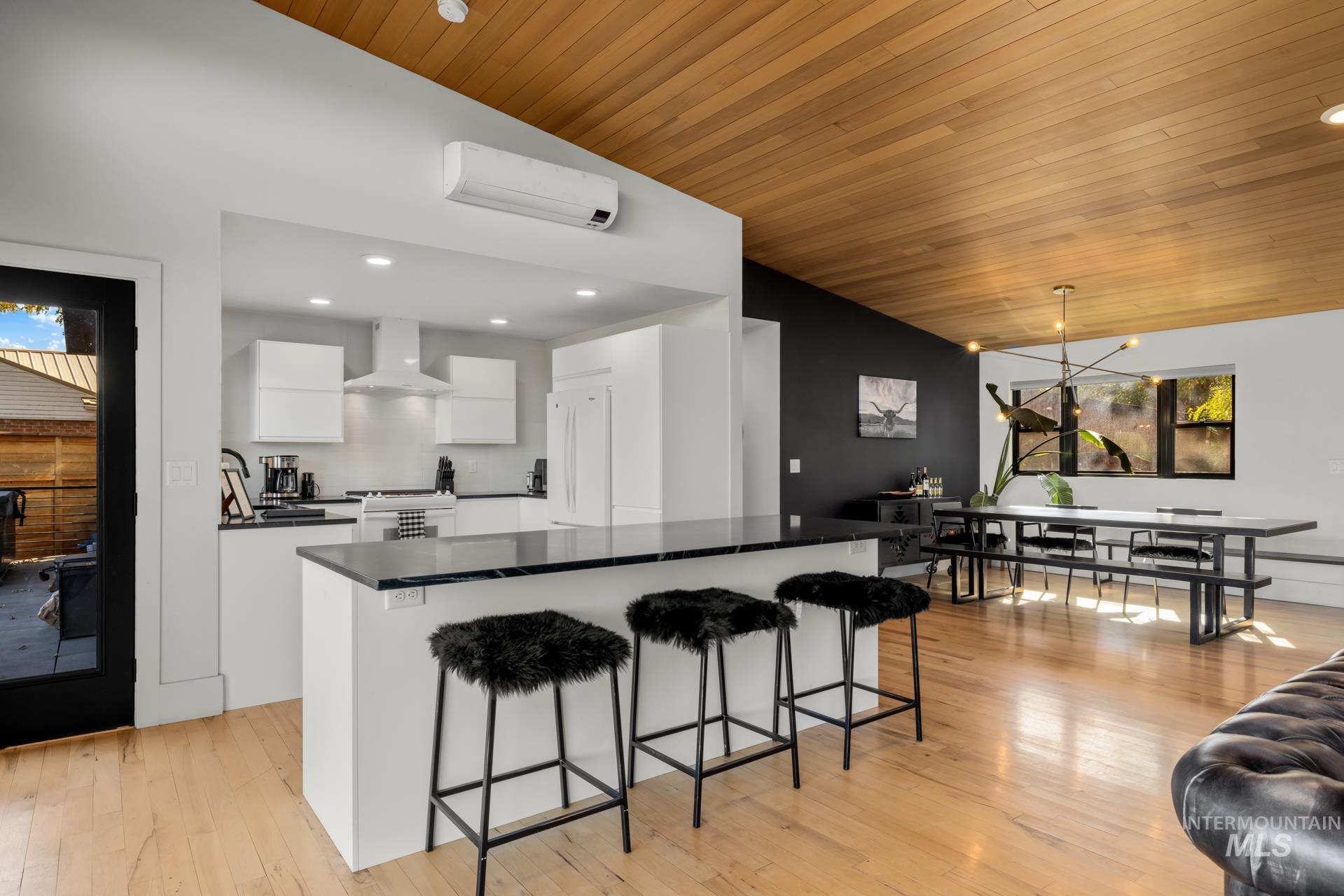 Kitchen with white cabinets, dark countertops, lofted ceiling, decorative light fixtures, and light wood-style flooring