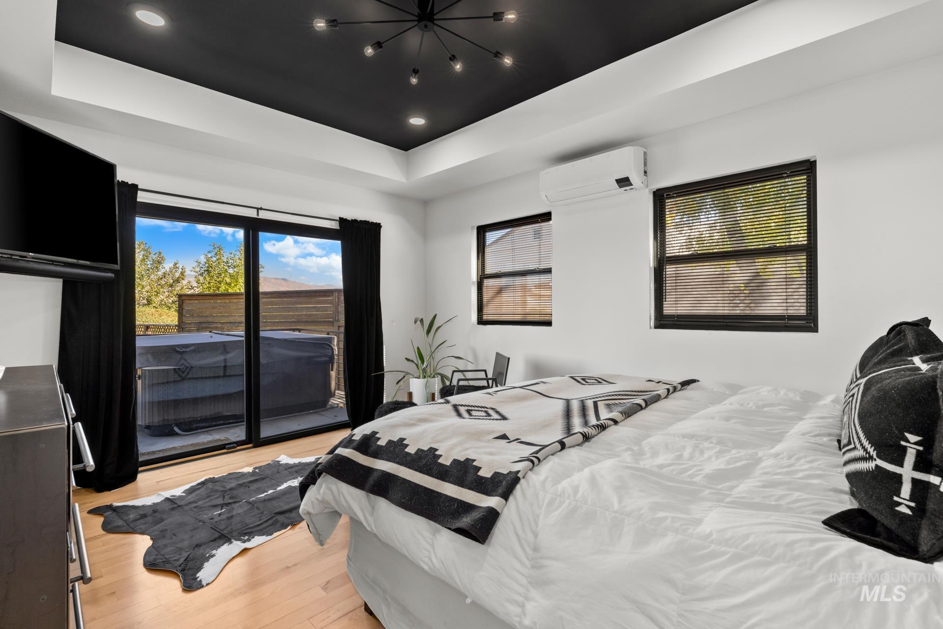Bedroom with access to exterior, light wood-style floors, a raised ceiling, recessed lighting, and an AC wall unit