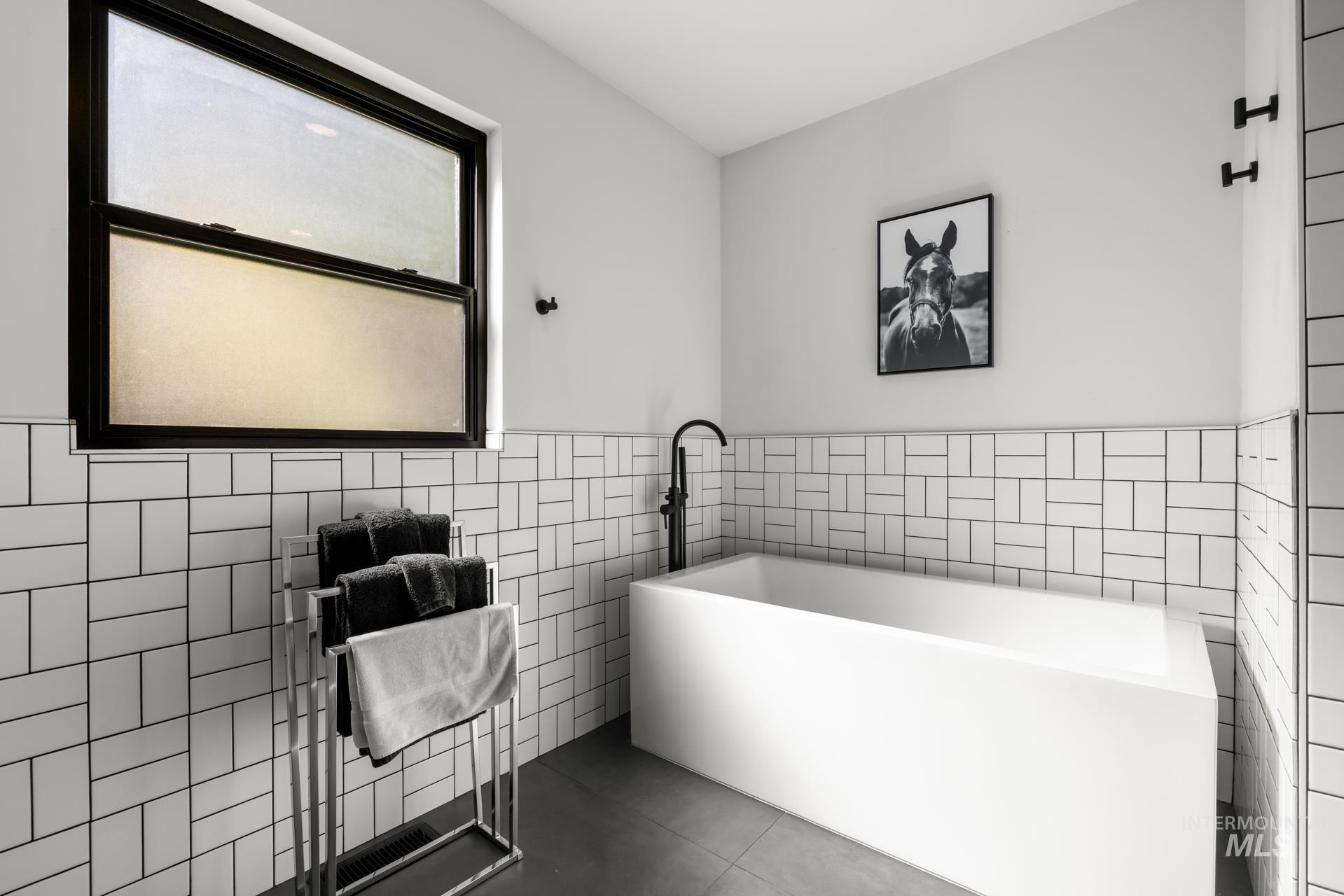 Full bathroom featuring tile walls, a freestanding bath, dark tile patterned floors, and wainscoting
