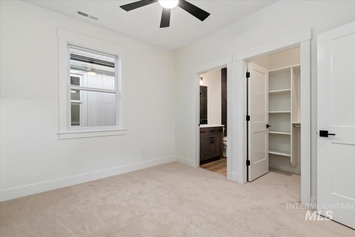 Unfurnished bedroom with light carpet, a spacious closet, ensuite bathroom, and ceiling fan