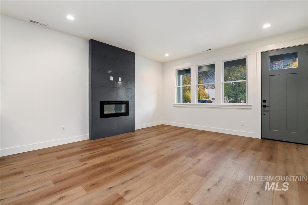 Unfurnished living room with light wood finished floors, a large fireplace, and recessed lighting