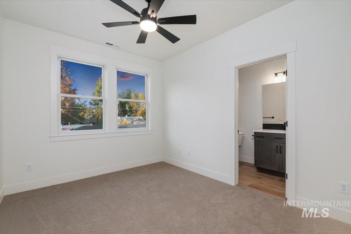 Unfurnished bedroom featuring light carpet, connected bathroom, and a ceiling fan
