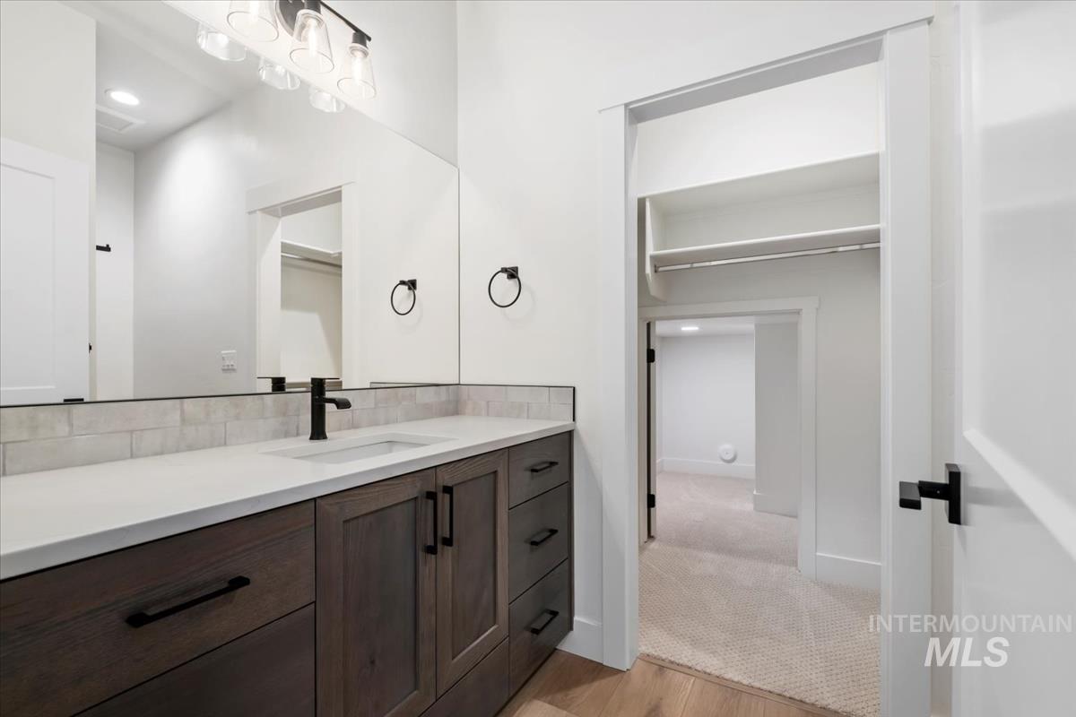 Bathroom with vanity, light wood-style floors, recessed lighting, a walk in closet, and tasteful backsplash