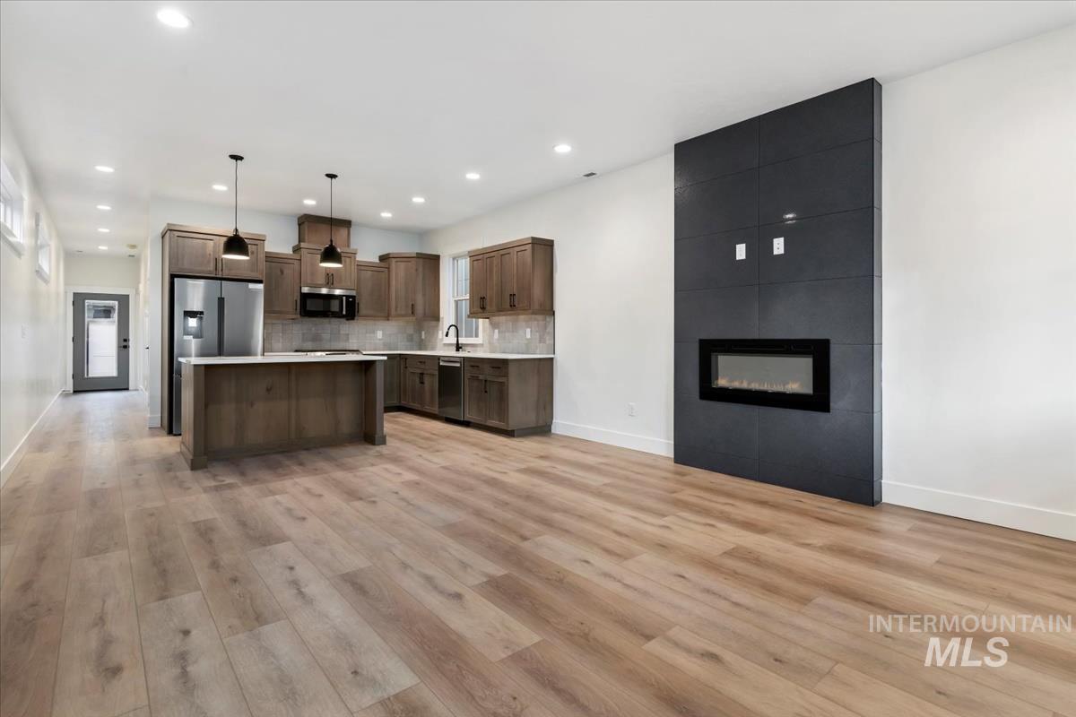Kitchen with hanging light fixtures, tasteful backsplash, light countertops, a kitchen island, and a large fireplace