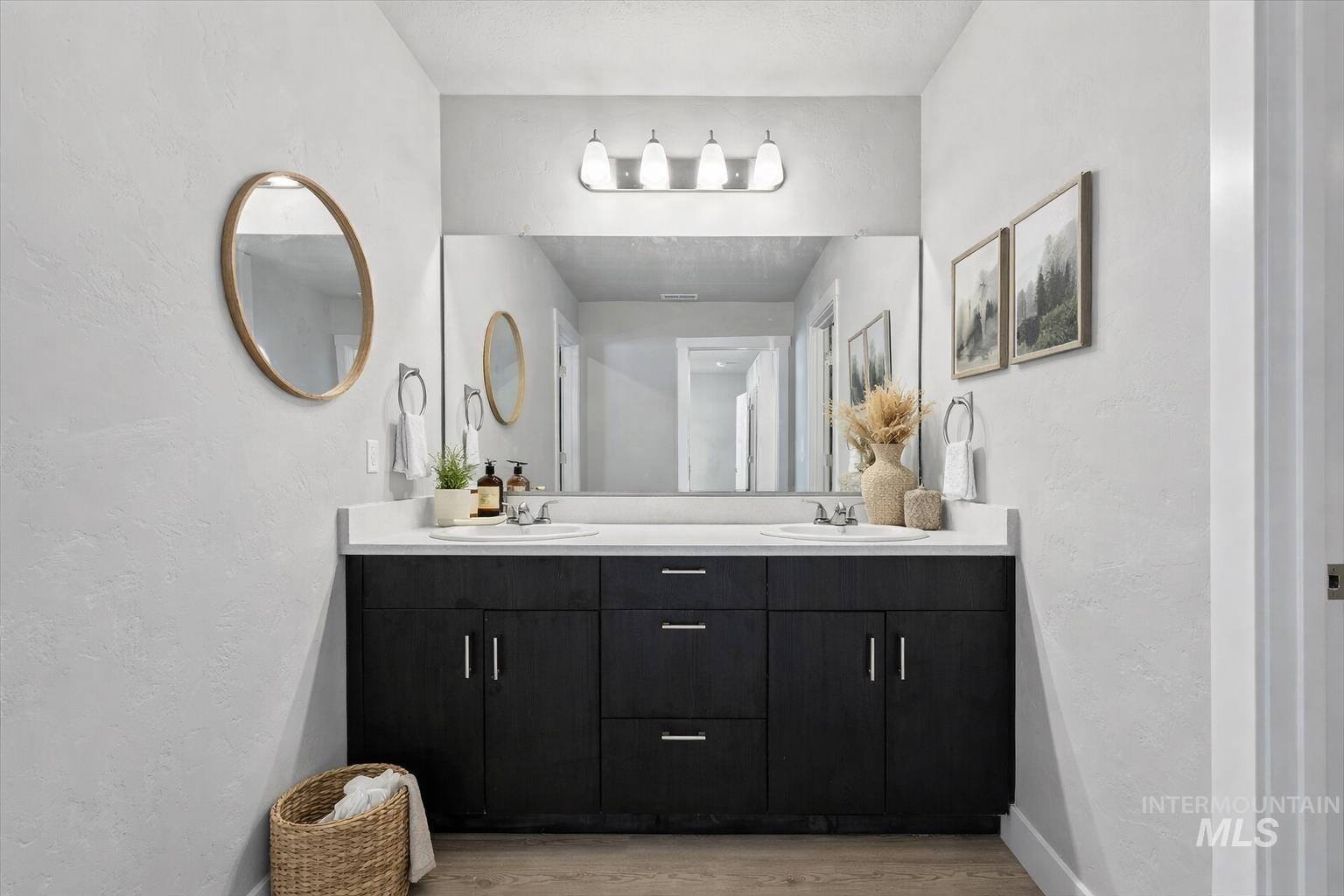 Full bath with a textured wall, double vanity, and light wood-style flooring