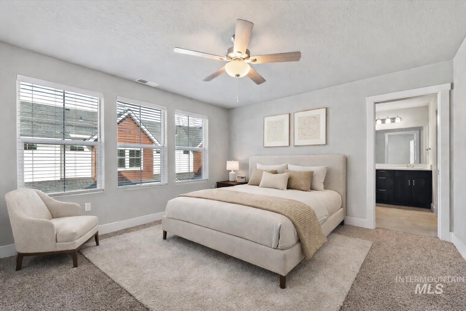 Carpeted bedroom with a textured ceiling, ceiling fan, and connected bathroom