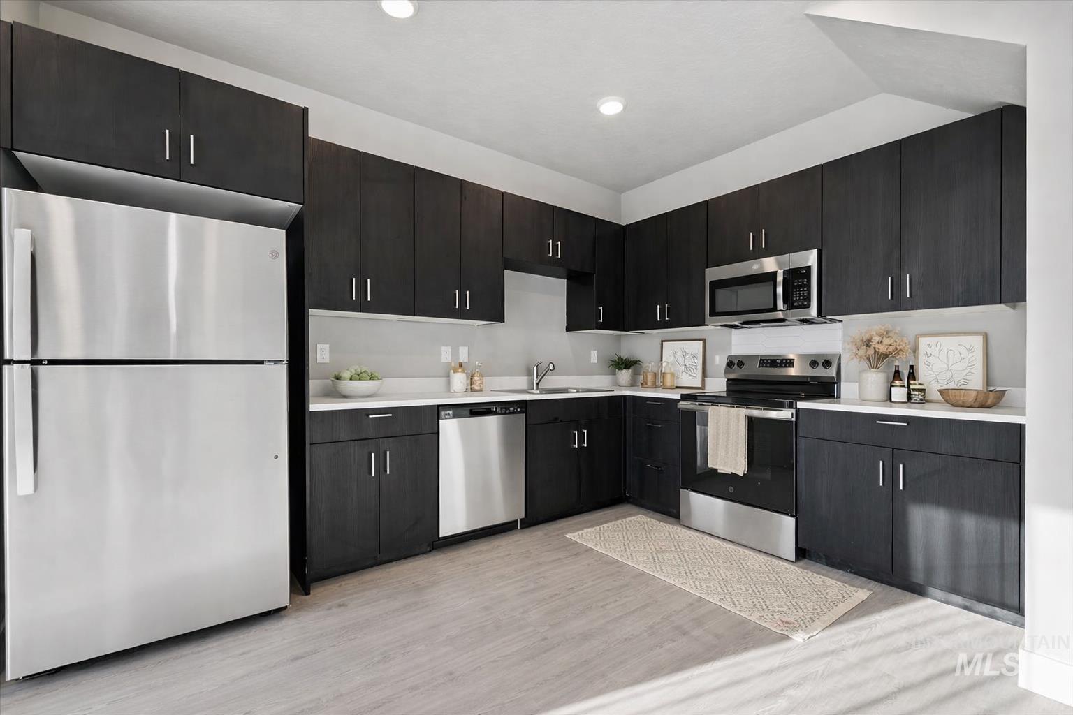 Kitchen featuring appliances with stainless steel finishes, dark cabinetry, and light wood finished floors