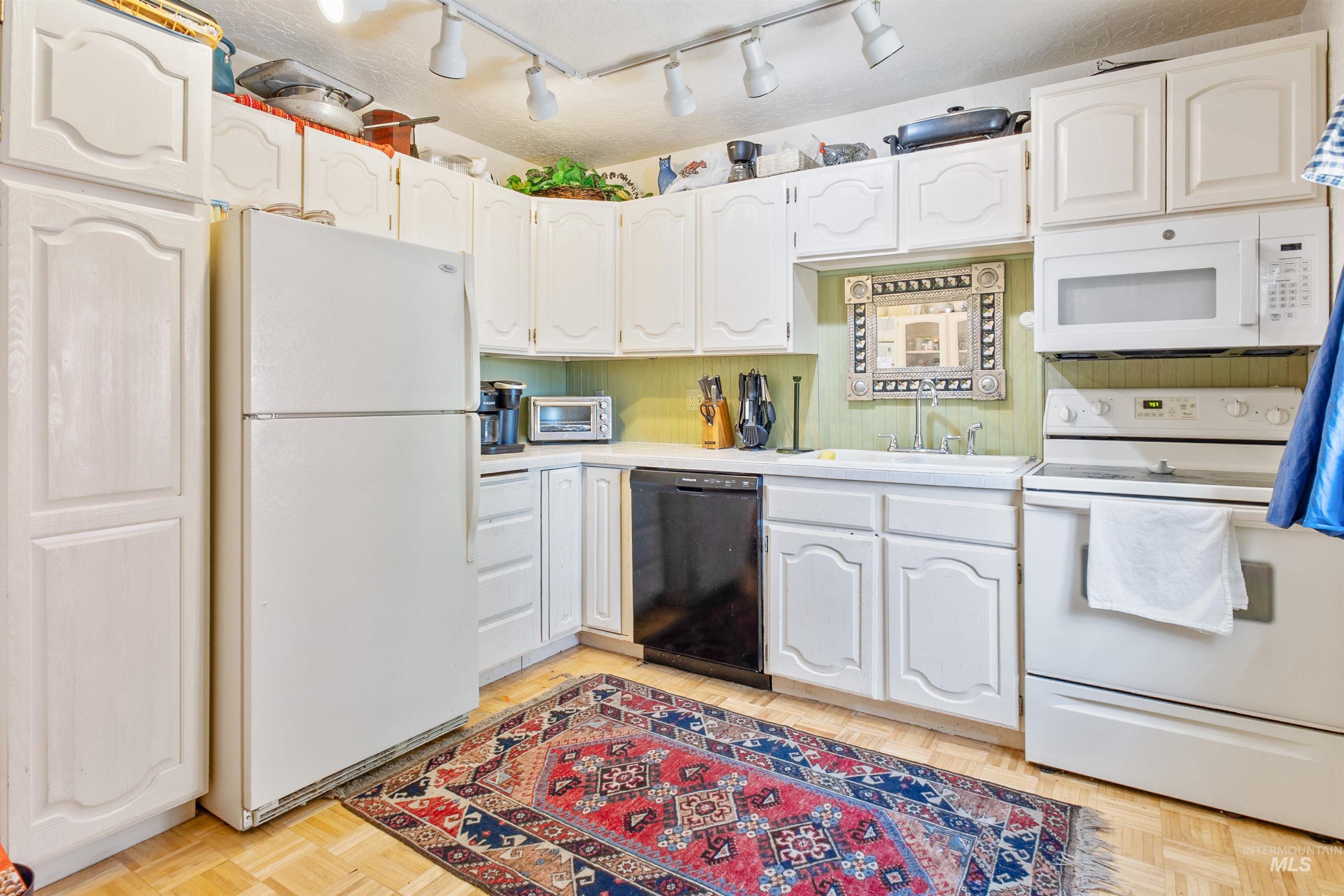 Kitchen with white appliances, light countertops, white cabinets, and rail lighting